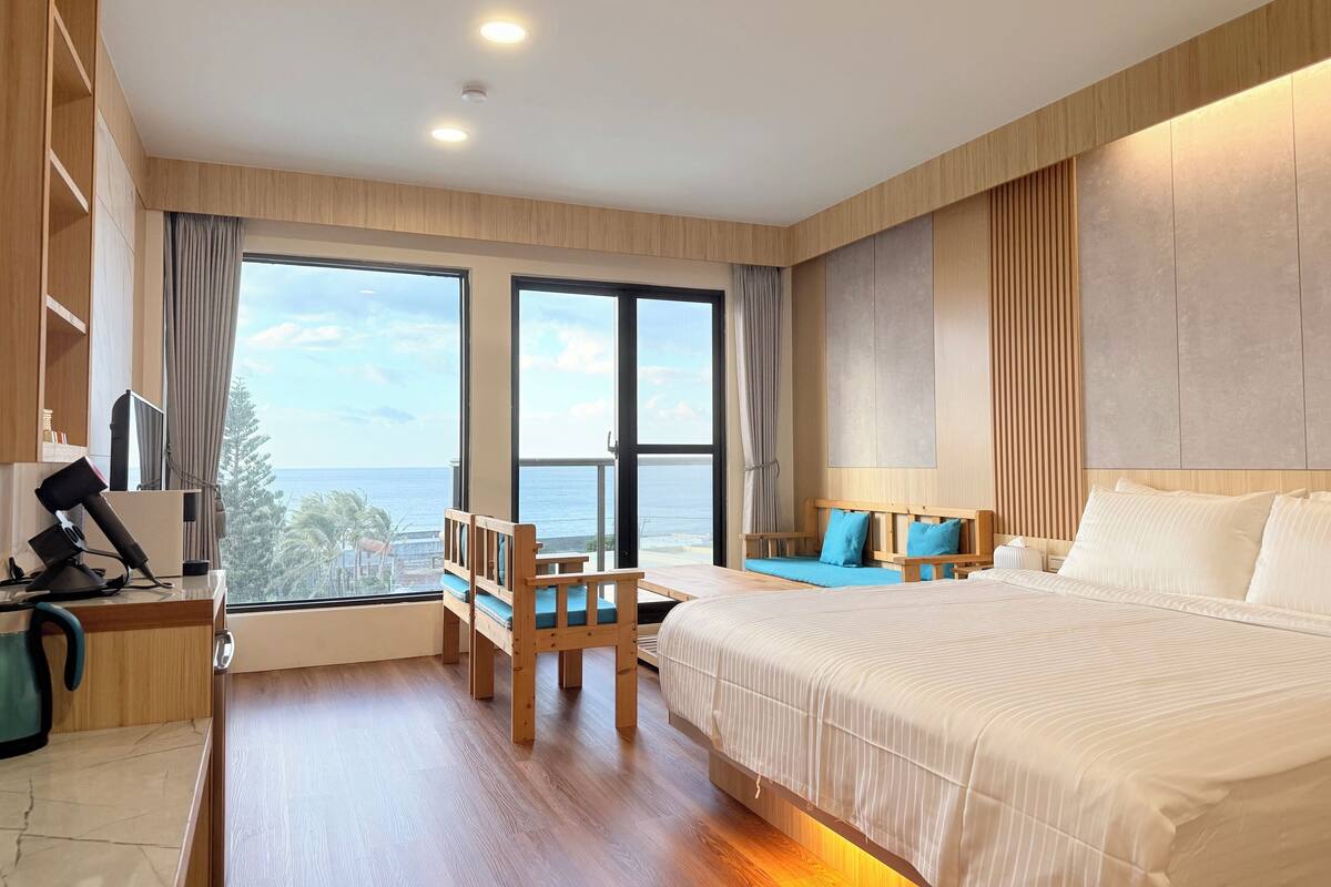 A hotel room with a large bed, a desk with a computer, a chair, and a view of the ocean.