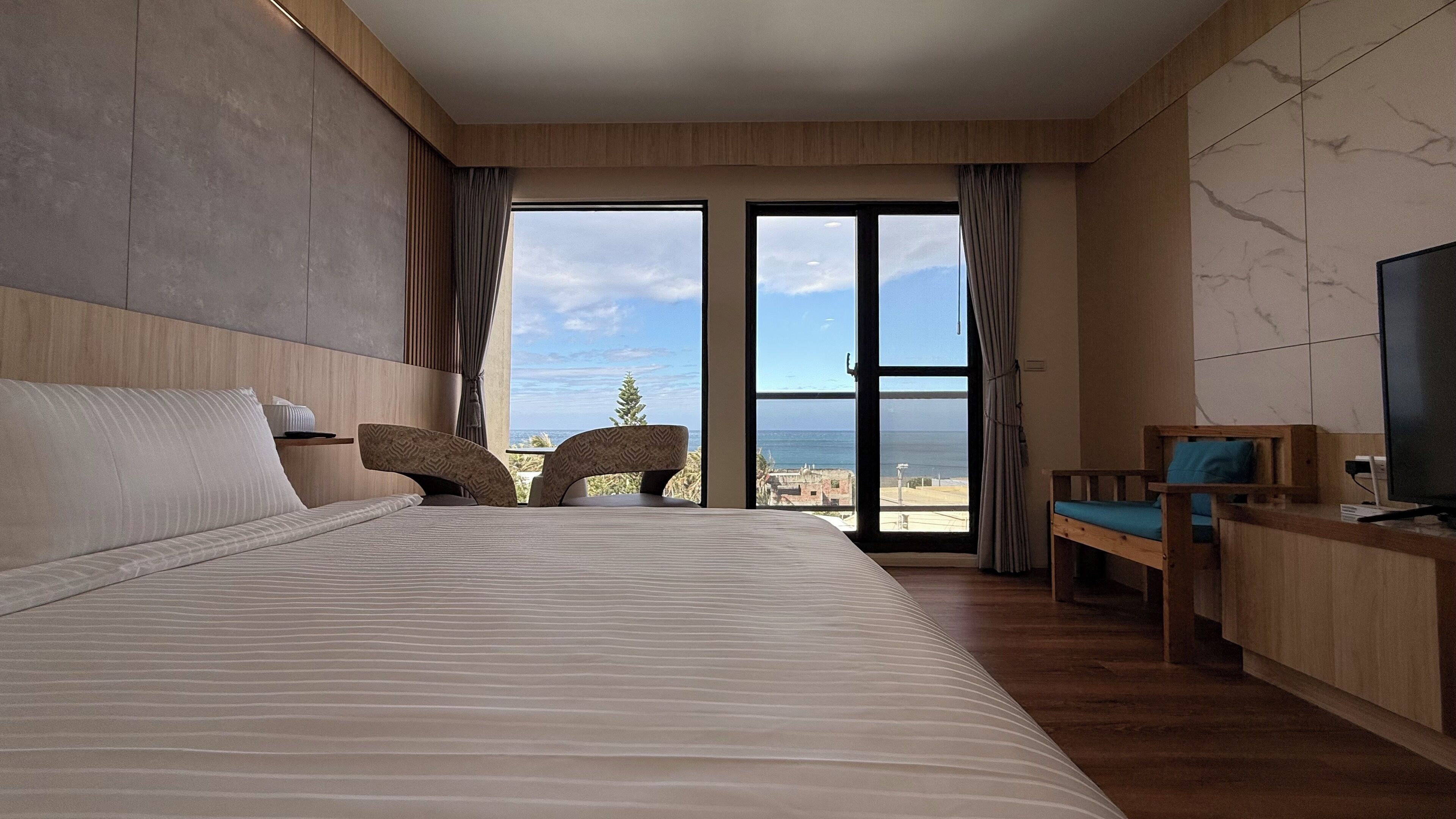 Una habitación de hotel moderna con una cama grande, un área de descanso con vistas al mar y un televisor.