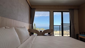 Ett hotellrum med en stor säng, två stolar, utsikt över havet och en balkong.
