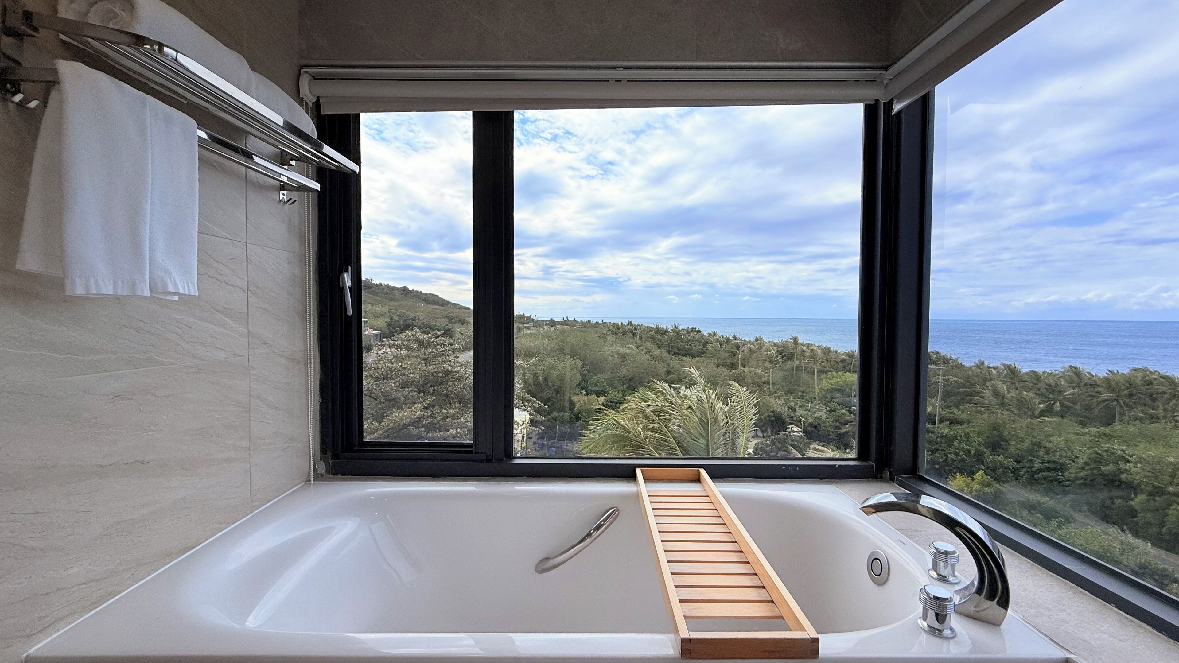 Uma casa de banho moderna com uma banheira grande, uma janela com vista para a paisagem costeira e um porta-toalhas.