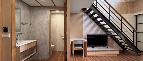 A modern bathroom with a wooden vanity, marble backsplash, and a built-in toilet. A wooden chair is placed near a fireplace. A staircase with a metal railing leads to an upper level.