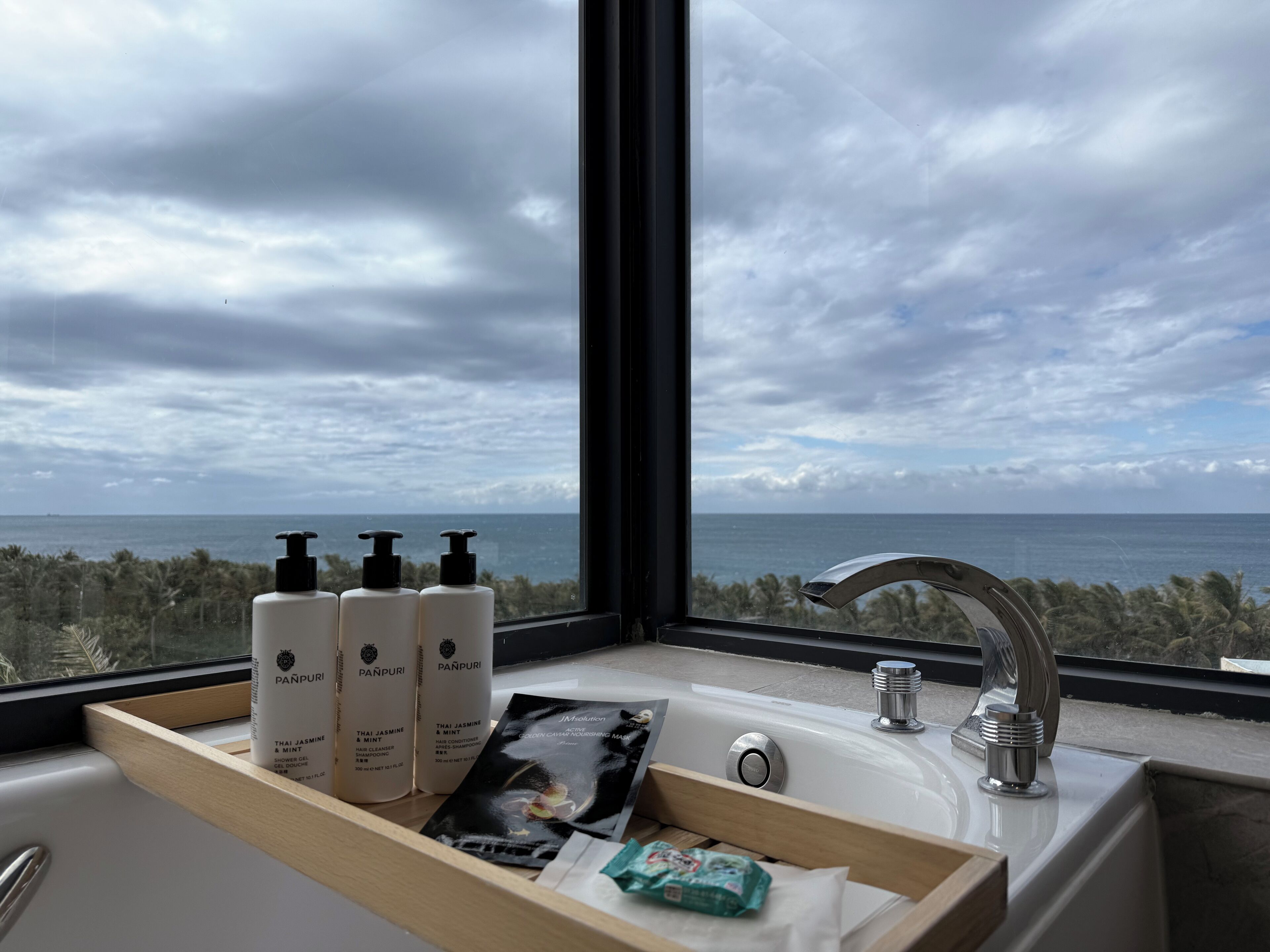Een badkamer met uitzicht op zee, een wastafel en drie flesjes haarverzorging van Panpuri.
