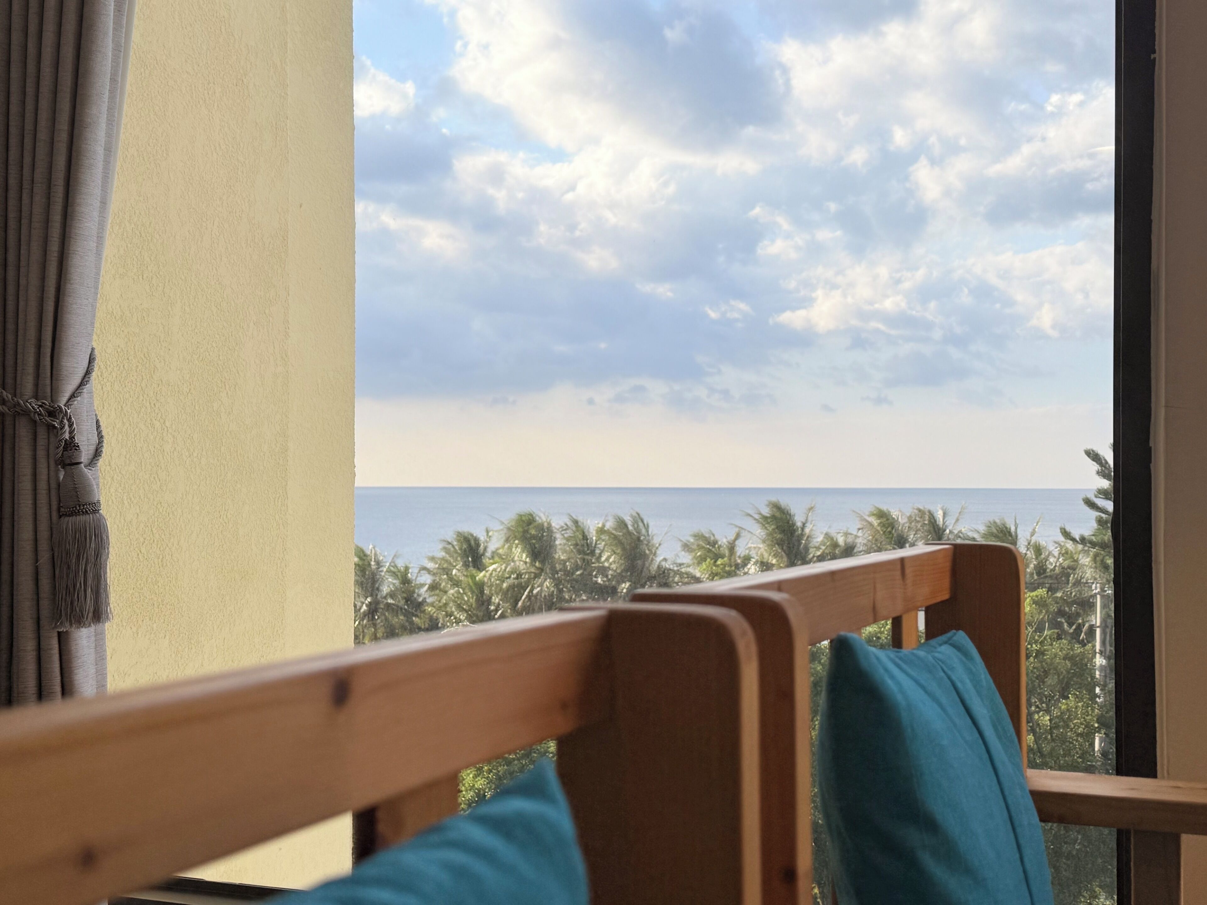 A room with a wooden bench, a view of the ocean, and a curtain.
