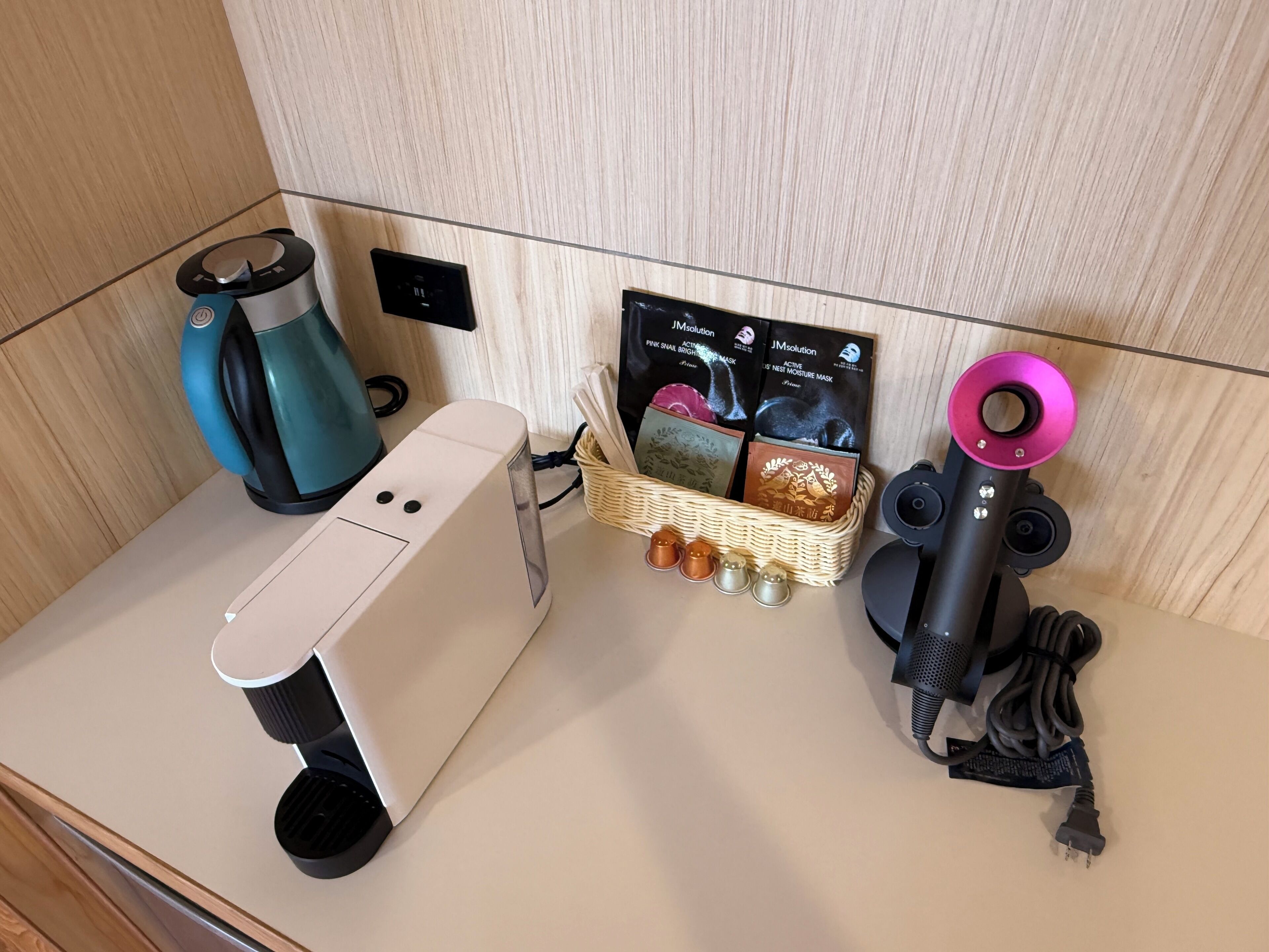 Una kitchenette con cafetera, hervidor de agua, secador de pelo y una cesta con cepillo de pelo y pañuelos de papel.
