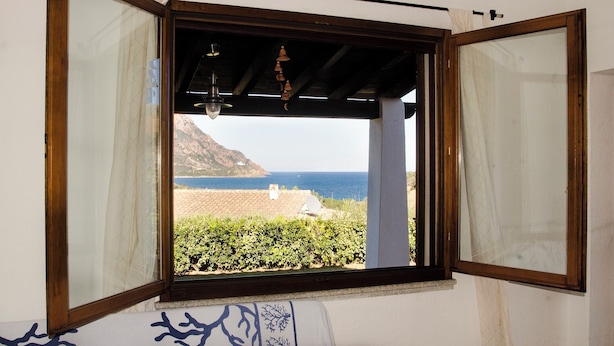 A room with a large window overlooking a coastal landscape, including a beach and mountains. - Villa with pool 300 meters from the sea - Ogliastra (Tertenia)