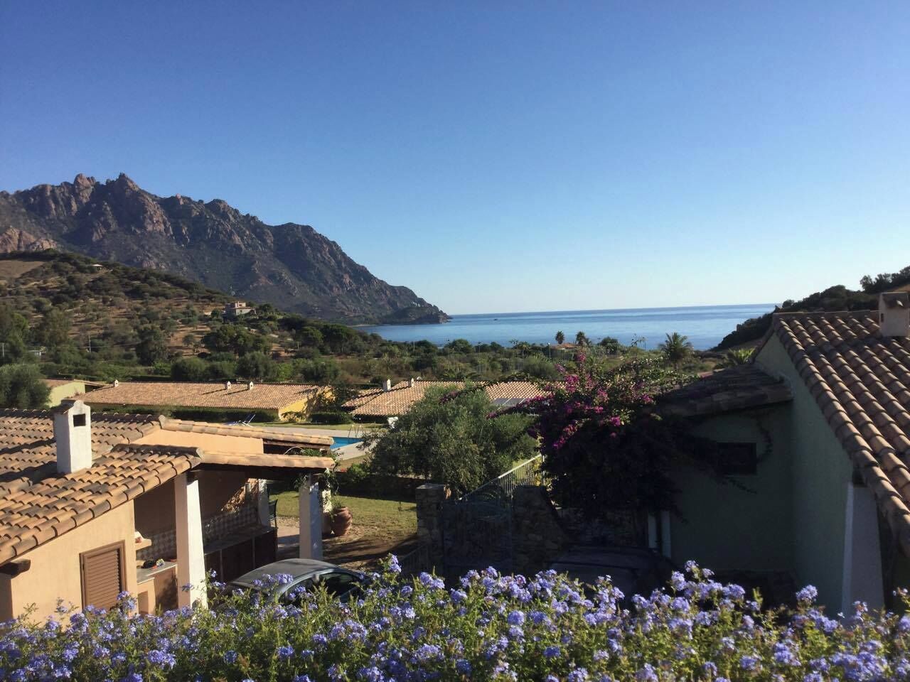 Eine Küstenvilla mit Terrakotta-Dächern, einem Swimmingpool und Blick auf das Meer und die Berge.