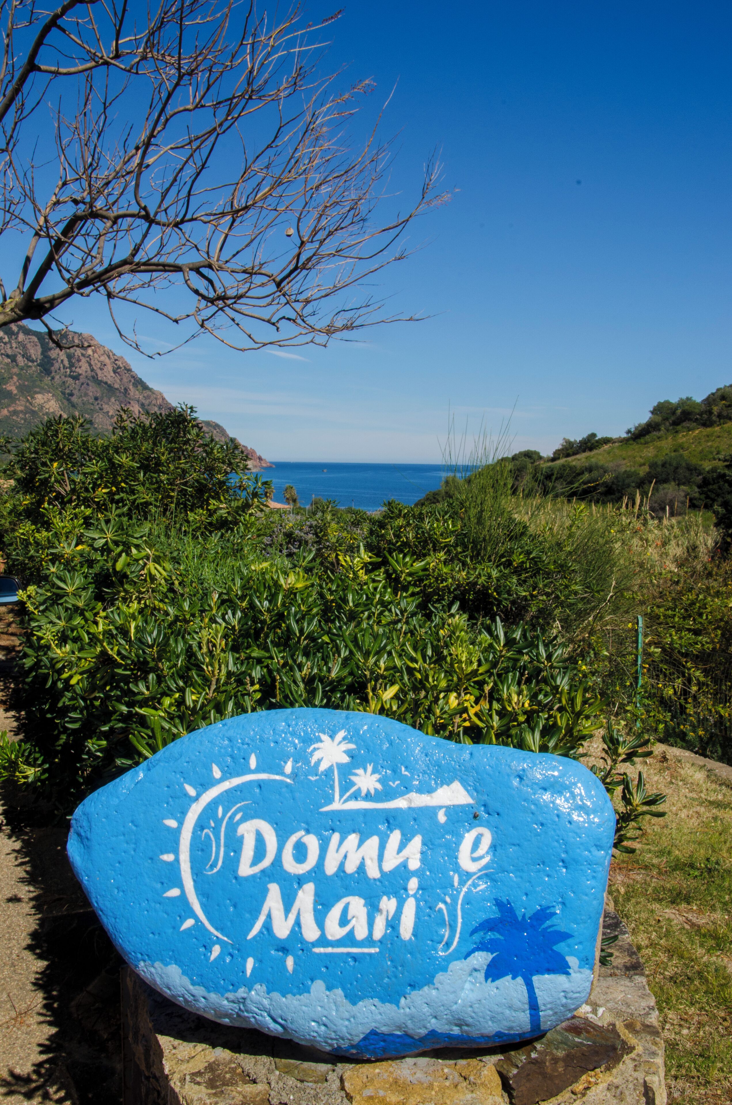 Une enseigne en pierre avec le nom « Domino’s » et des motifs de palmiers, placée sur un fond représentant un paysage côtier avec un ciel dégagé.