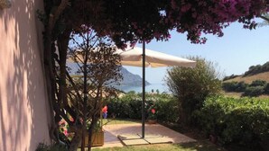 A patio area with a beige umbrella, a small tree with pink flowers, and a view of the sea in the background. - Villa with pool 300 meters from the sea - Ogliastra (Tertenia)