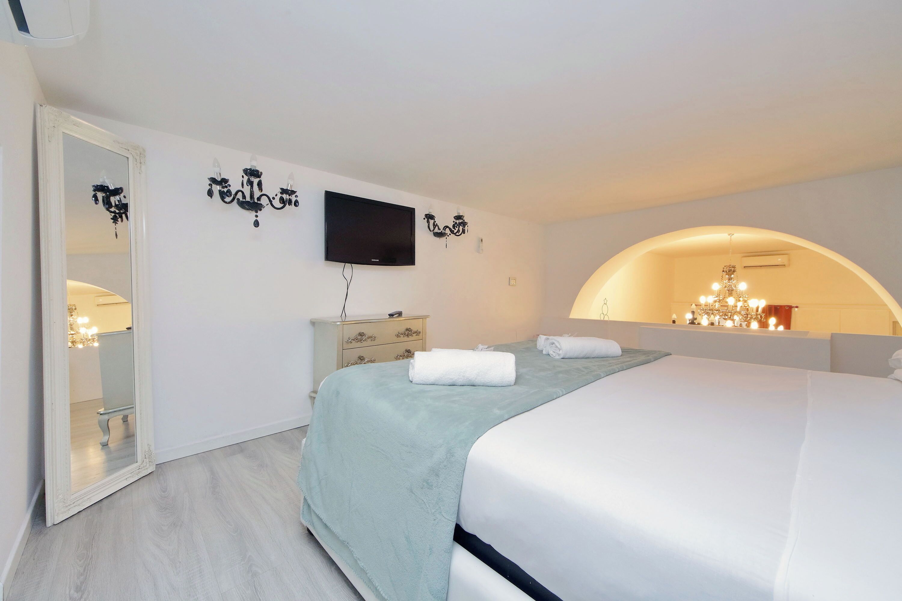 A bedroom with a bed, a TV, a dresser, and a mirror.