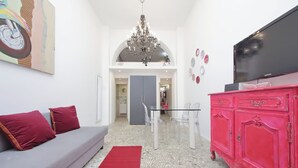 Een woonkamer met een grijze bank, rode kussens, een rood vloerkleed, een roze kast en een televisie op een standaard.