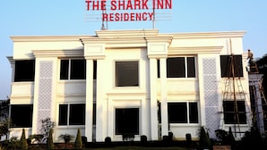 Un hotel chiamato "The Shark Inn Residency" con uno stile architettonico classico, caratterizzato da finestre simmetriche e pannelli decorativi.