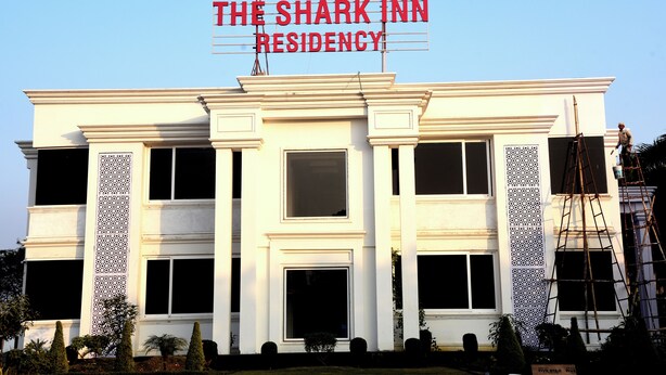Un hôtel appelé « The Shark Inn Residency », de style architectural classique, se distinguant par ses fenêtres symétriques et ses panneaux décoratifs.