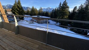 Een balkon met uitzicht op een met sneeuw bedekte grond, een gebouw en besneeuwde bergtoppen.