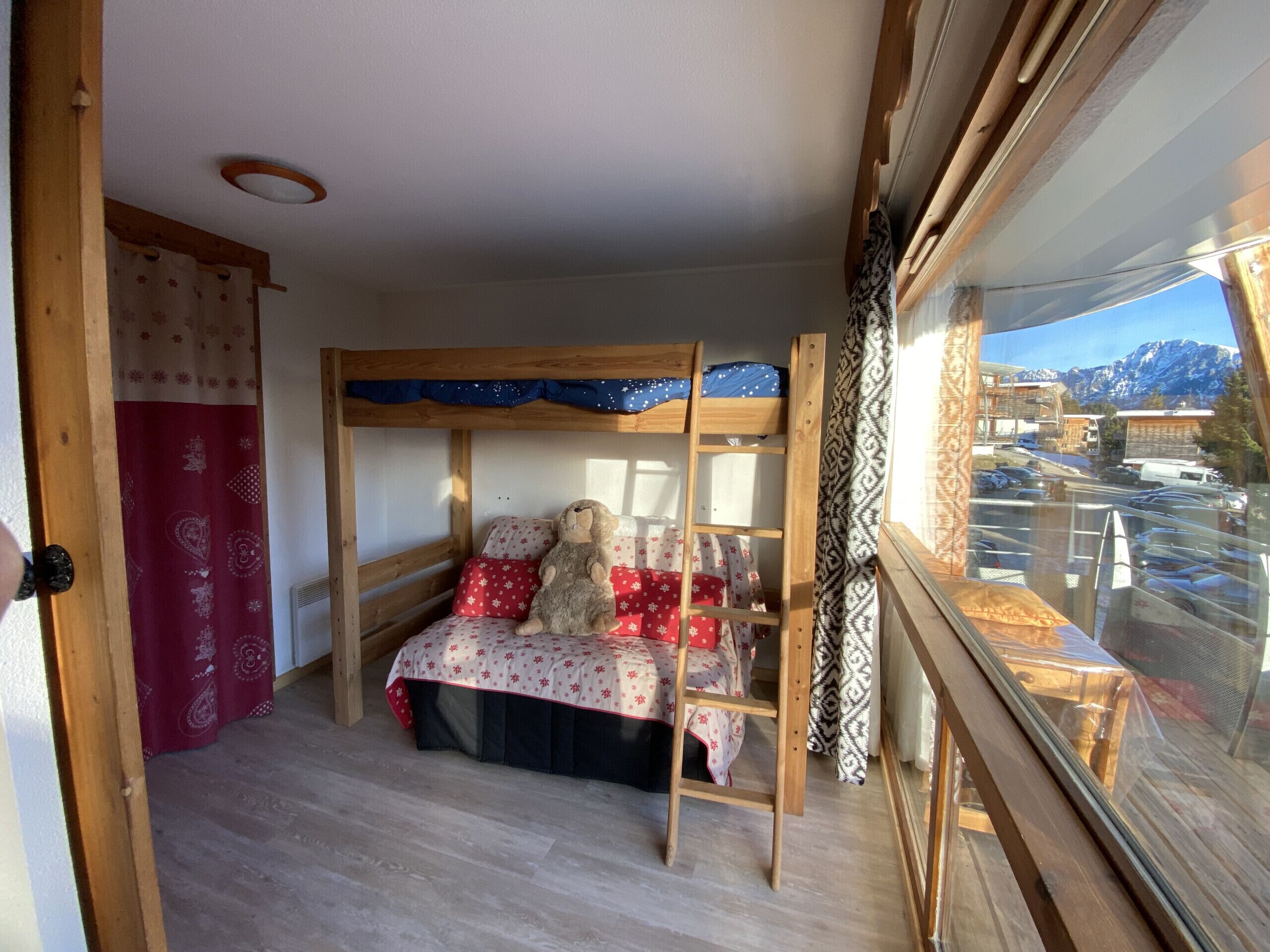 A room with a bunk bed, a window with a view of a mountain, and a wooden ceiling.