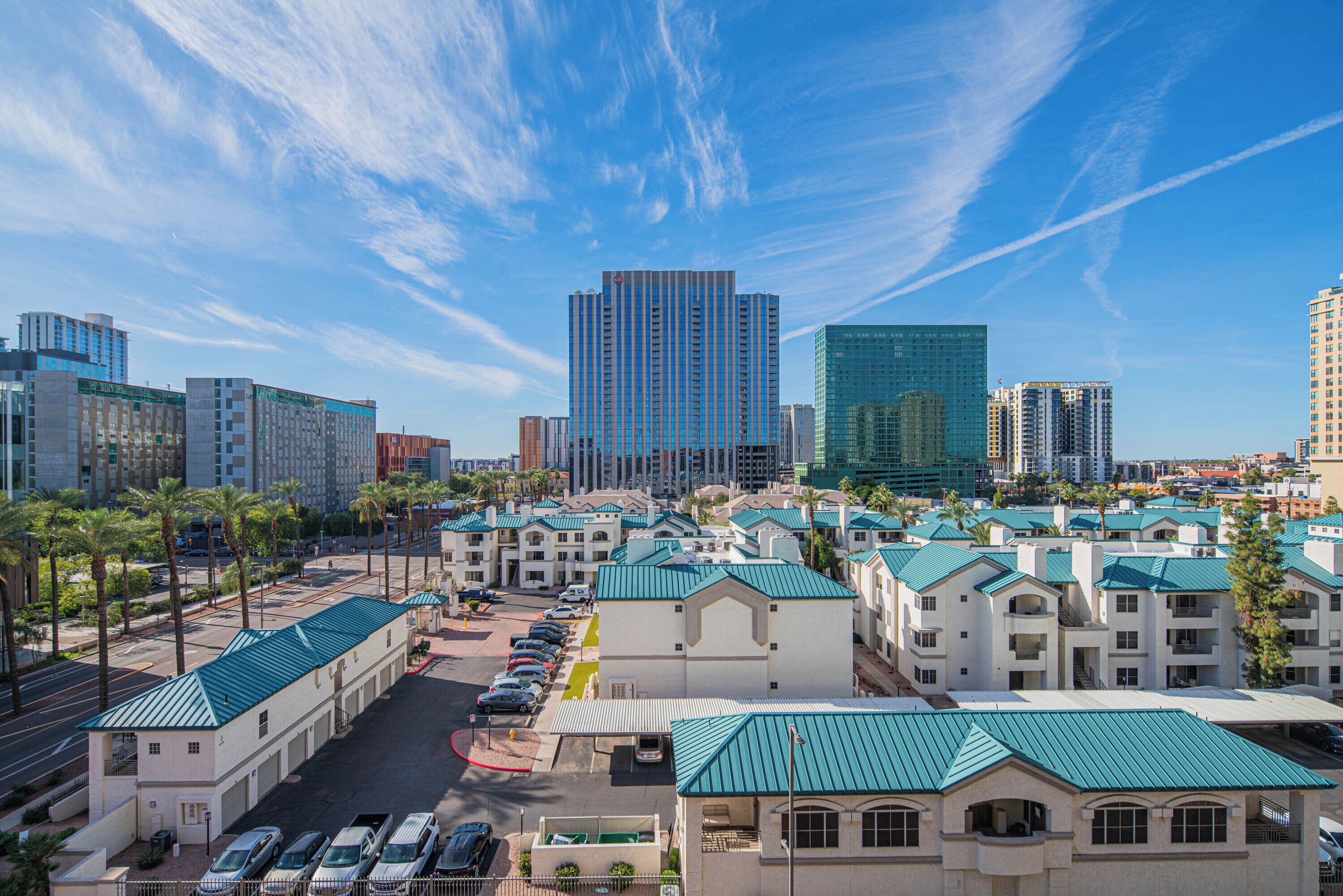 A hotel with a row of parking spaces, a green-roofed building, and a clear blue sky.