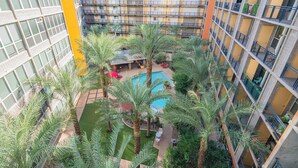 Een hotel met meerdere verdiepingen, inclusief een zwembad op het dak, omgeven door palmbomen en terrasjes.