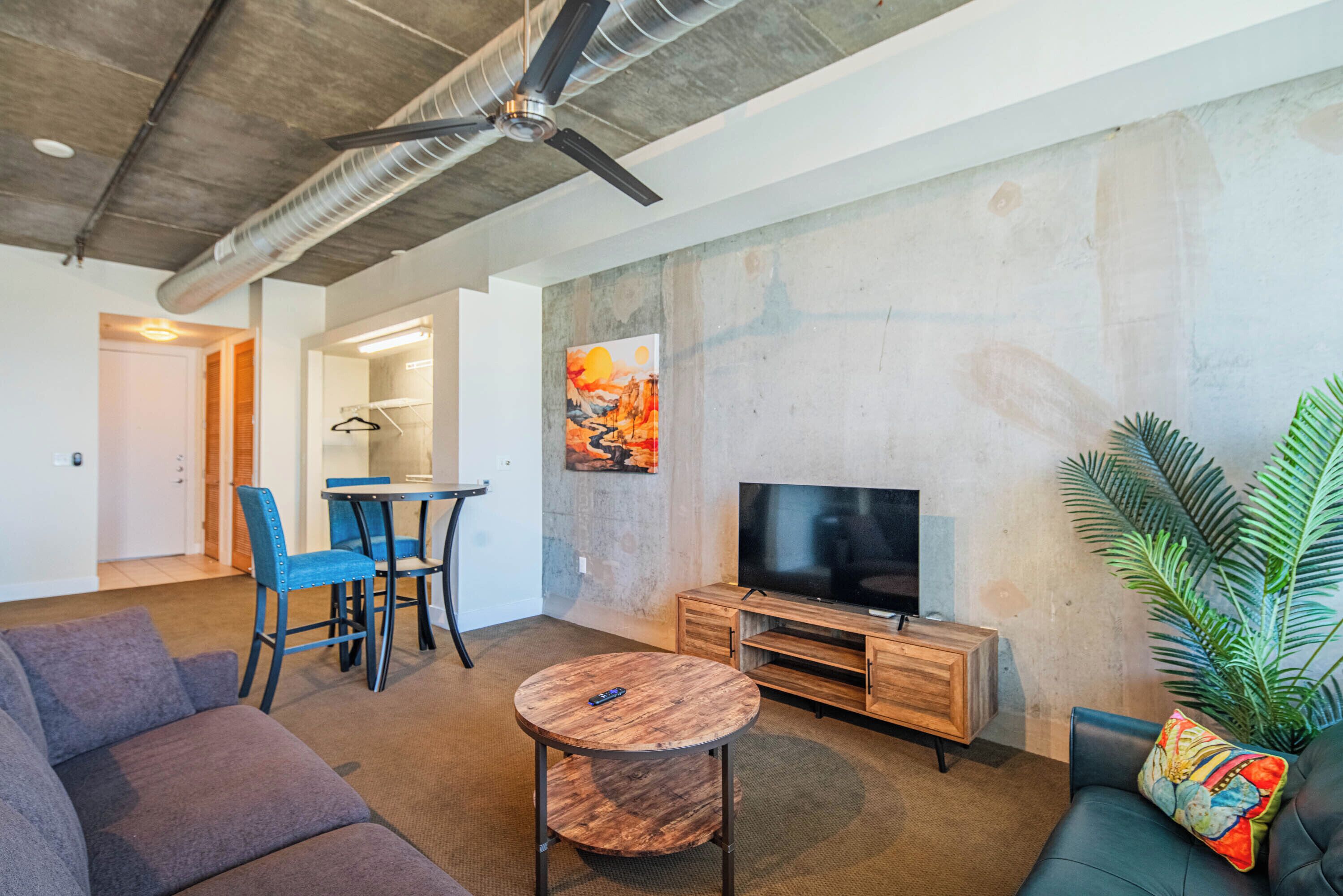 A modern living room with a sofa, a round coffee table, a TV, and a dining area with chairs and a table.