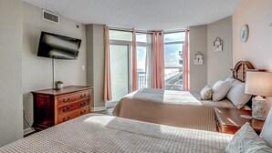 Habitación de hotel con dos camas, televisión, cómoda, ventana con cortinas y vista a la ciudad.