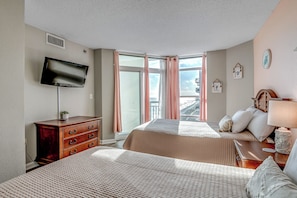 Ein Hotelzimmer mit zwei Betten, einem Fernseher, einem Schminktisch und einem Fenster mit Vorhängen, mit Blick auf die Stadt.
