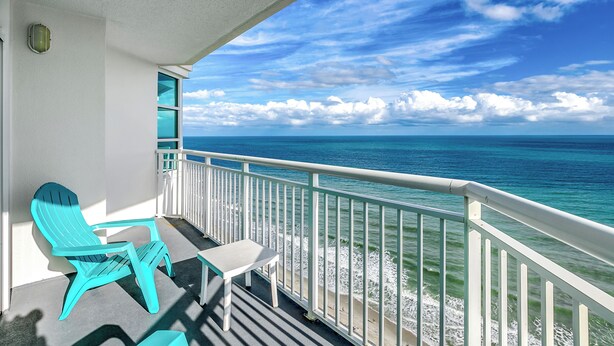 Un balcone con sedie color turchese e un tavolo con vista su una spiaggia, onde e cielo sereno.