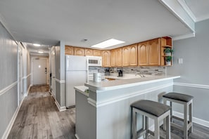 A modern kitchen with wooden cabinets, a white countertop, and a built-in microwave. - Palms Resort #1704: 2 BR, 2.5 BA Condominium in Myrtle Beach, Sleeps 6 (Myrtle Beach)