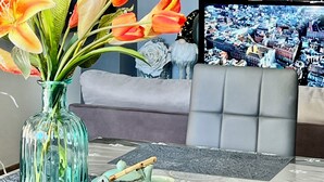 Ein Wohnzimmer mit einer Glaskaraffe voller Blumen, einem Sofa, einem Fernseher und einem Tisch mit Teekanne und Tassen.