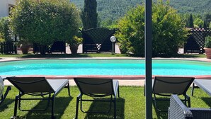 Ein Schwimmbad mit Liegestühlen, einer Pergola und Blick auf einen bewaldeten Hügel.