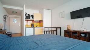 A compact hotel room with a bed, kitchenette, and a TV mounted on the wall. - Studio équipé 2 pers en centre ville (Agde)