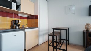 Ett kompakt kök med en kaffebryggare, ett litet kylskåp och en pall.