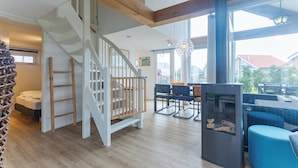 A spacious living area with a wooden staircase, a fireplace, and a large window offering a view of the outside. - Coastal Family Escape With Enclosed Garden (Renesse)