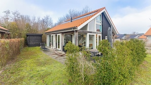 A modern house with a sloped roof, large windows, and a patio area with outdoor furniture. - Coastal Family Escape With Enclosed Garden (Renesse)
