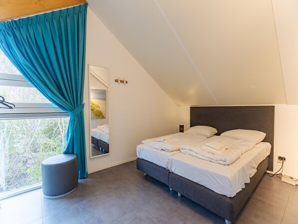 Une chambre moderne avec un grand lit, une table de chevet, une fenêtre avec des rideaux et une vue sur la verdure.