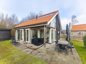Een modern huis met een glazen uitbouw, een terras met tuinmeubilair en een hangmat.