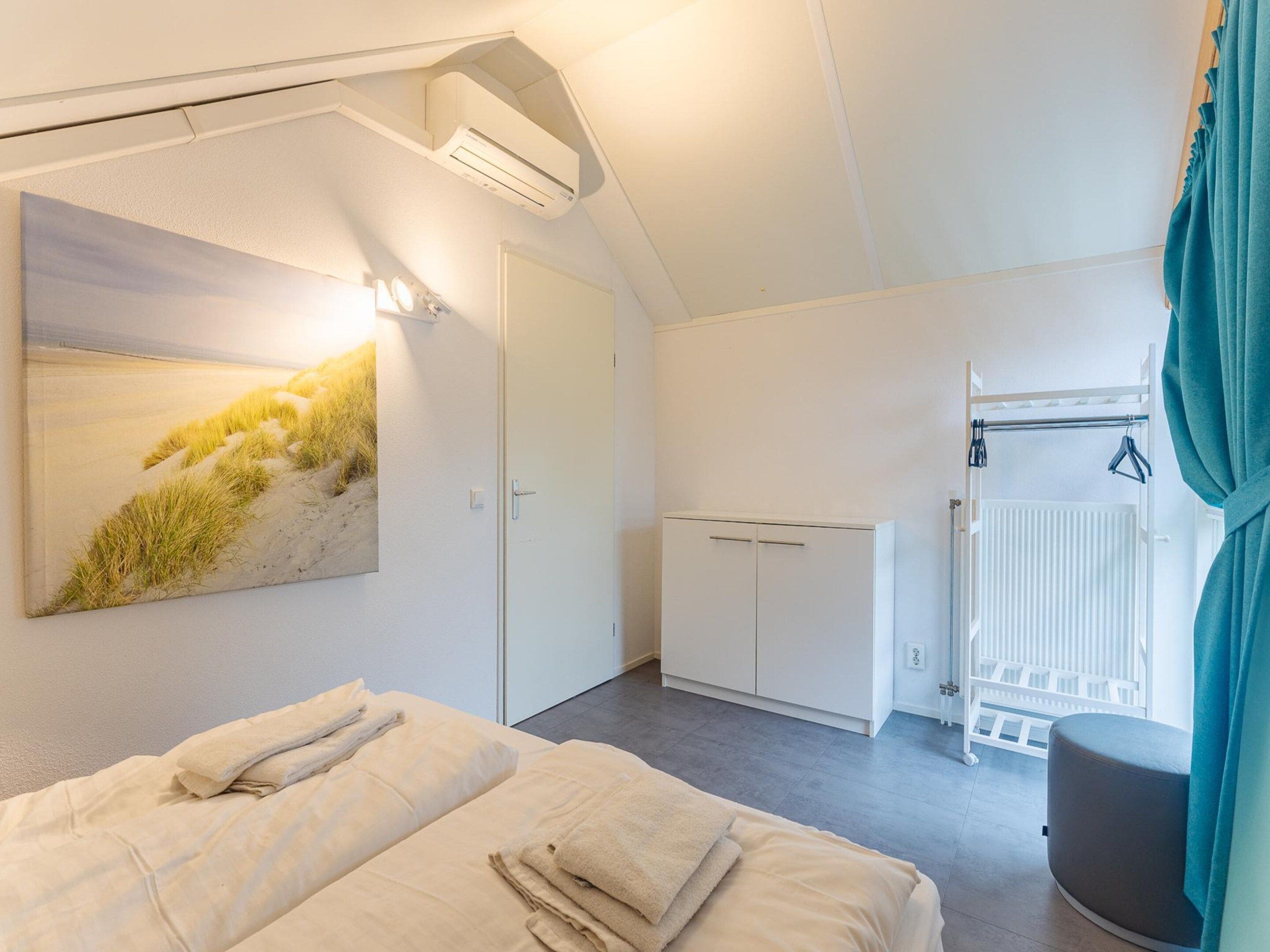 A bedroom with a bed, a wardrobe, a radiator, and a painting of a beach scene.