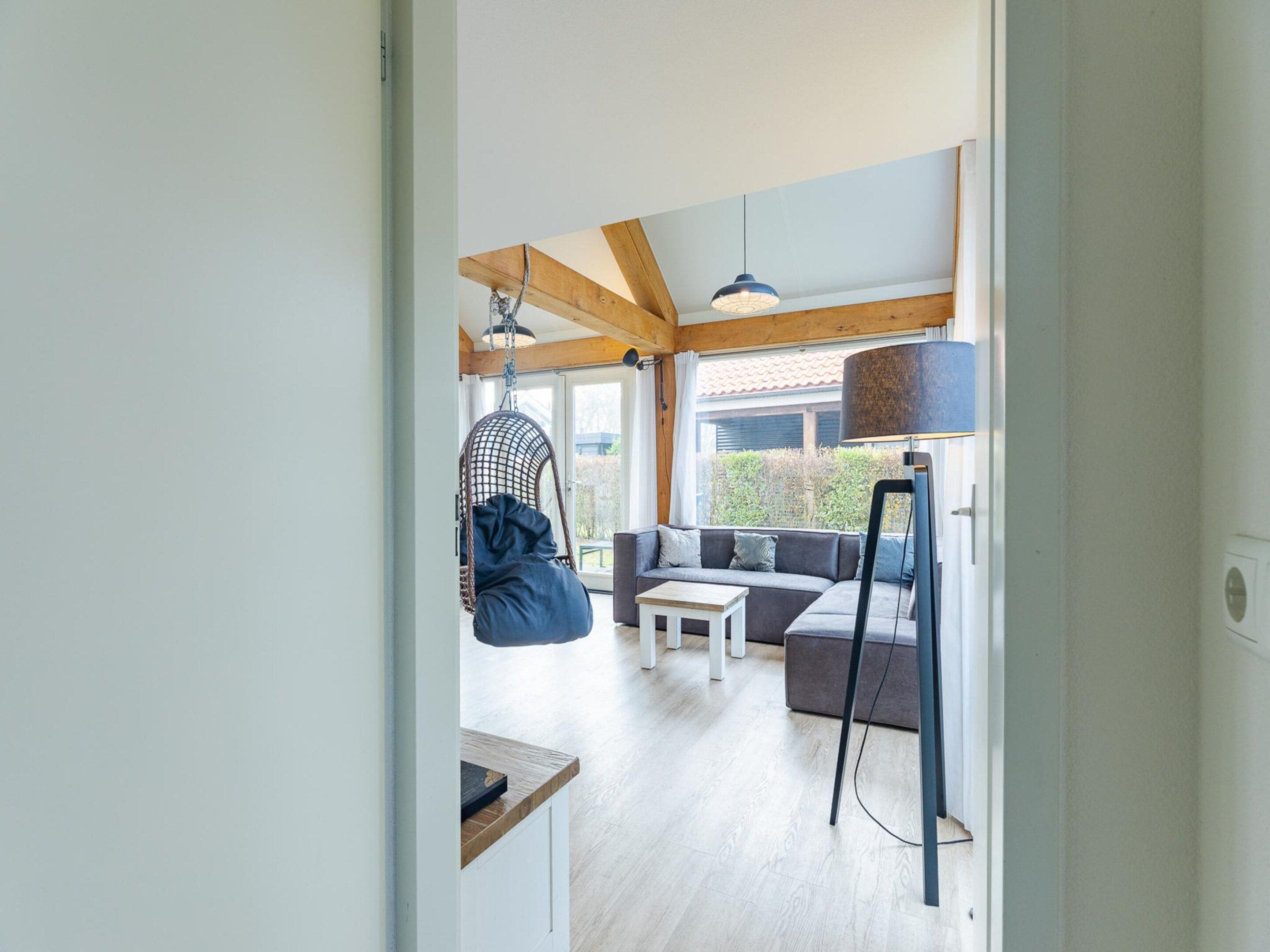 A modern interior with a wooden ceiling, a hanging chair, a sofa, a coffee table, and a floor lamp.