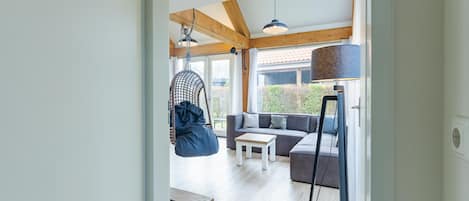 A modern interior with a wooden ceiling, a hanging chair, a sofa, a coffee table, and a floor lamp.