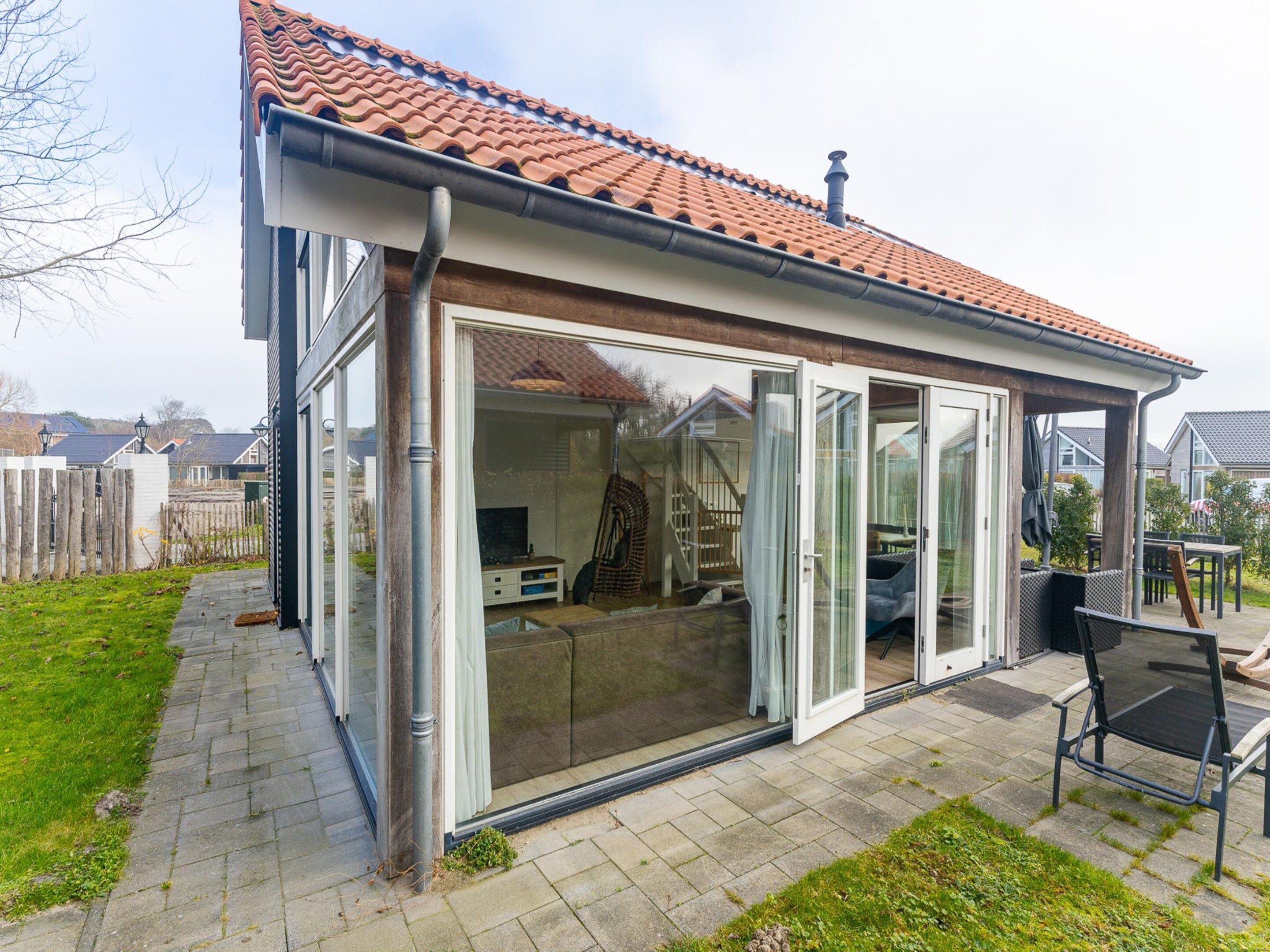 Et moderne hus med tegltag, store skydedøre i glas og en terrasse med udendørs møbler.