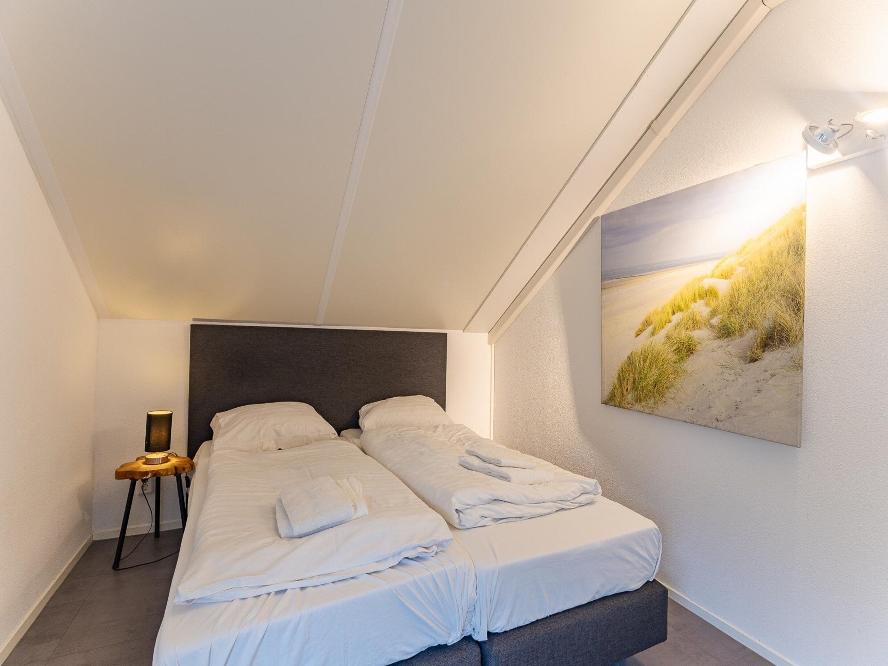 A bedroom with a bed, a bedside table, a lamp, and a wall-mounted artwork.