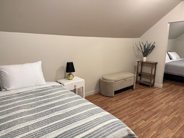 A bedroom with a bed, bedside table, lamp, bench, and a small wooden shelf. - Cozy 3-bedroom house in Duncan SC (Duncan)