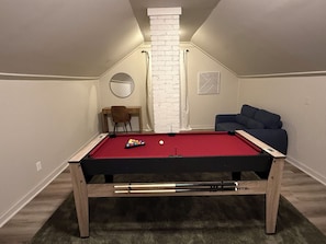 Une table de billard dans une pièce dont le plafond est en pente, avec un petit bureau, une chaise et un canapé.