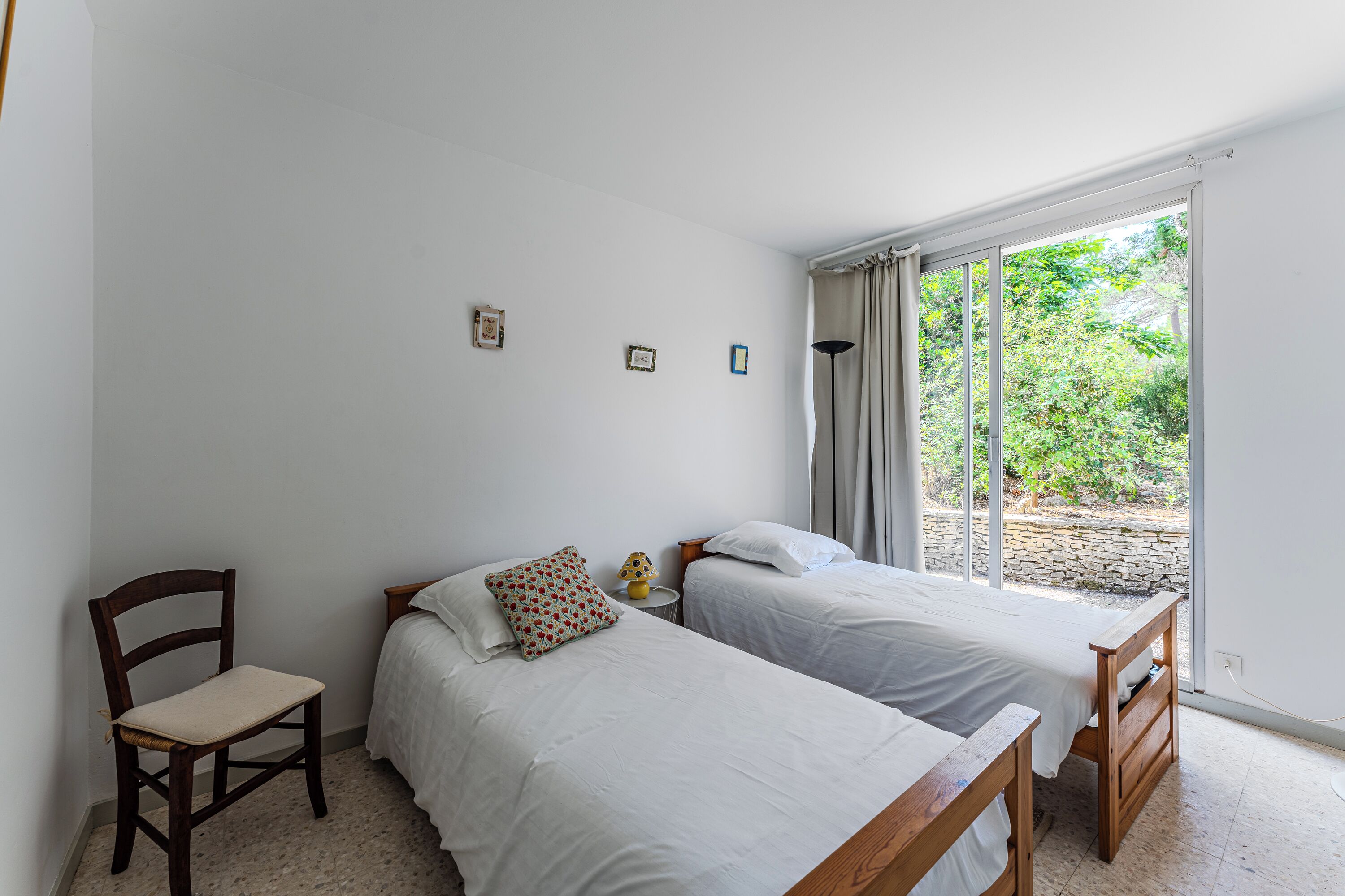 A bedroom with two beds, a chair, and a window with curtains.