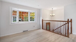 A spacious room with a large window, a wooden staircase, and a chandelier. - This house is a 3 bedroom(s), 2 bathrooms, located in Latham, NY. (Latham)