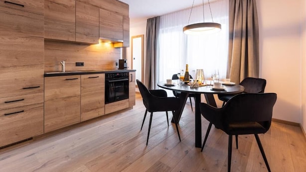 A modern kitchen with wooden cabinets, a dining table with chairs, and a large window with curtains. - AFOCH FEI das Landhaus (Sankt Anton am Arlberg)