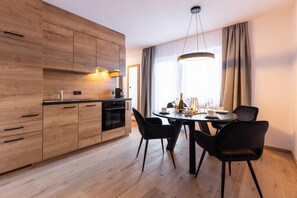 A modern kitchen with wooden cabinets, a dining table with chairs, and a large window with curtains. - AFOCH FEI das Landhaus (Sankt Anton am Arlberg)