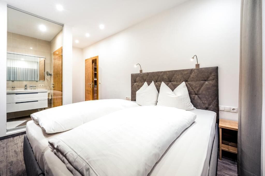 A modern hotel room with a large bed, a wooden headboard, a bedside table, and a mirror.