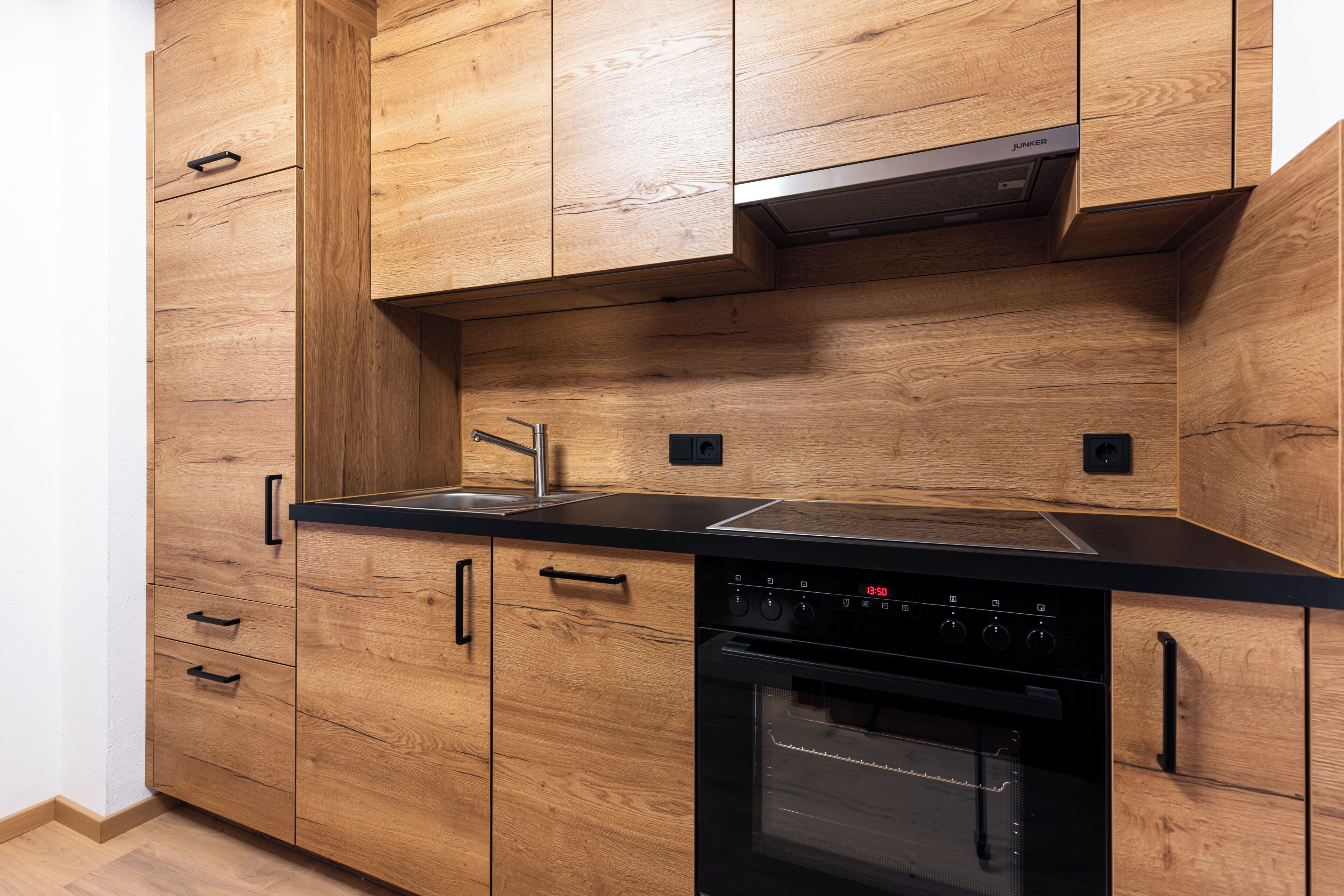 A kitchen with wooden cabinets, a black countertop, a stainless steel sink, and a built-in oven.