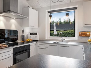 Eine moderne Küche mit einer großen Kochinsel, Edelstahlgeräten und einem Fenster mit Blick auf ein Haus und Bäume.