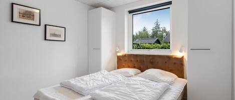 Une chambre à coucher avec un lit, une fenêtre donnant sur des maisons et deux tableaux encadrés accrochés au mur.
