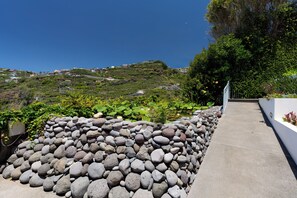 A pathway lined with a stone wall and greenery, leading to a hillside with houses. - Sea Sky House By Holiday Rental Madeira (Ribeira Brava)