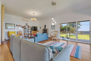 A living room with a sofa, armchairs, a coffee table, and a bookshelf. There is a large window with a view of the outdoors. - Sea Sky House By Holiday Rental Madeira (Ribeira Brava)